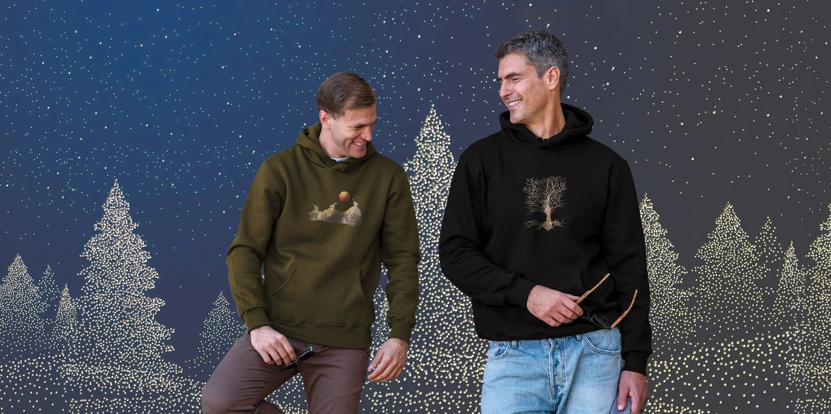 Two men in ZOE hoodies with original art, standing before festive lit Christmas trees