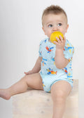 Baby in light blue airplane-print bodysuit from ZOE Crete, holding a yellow lemon